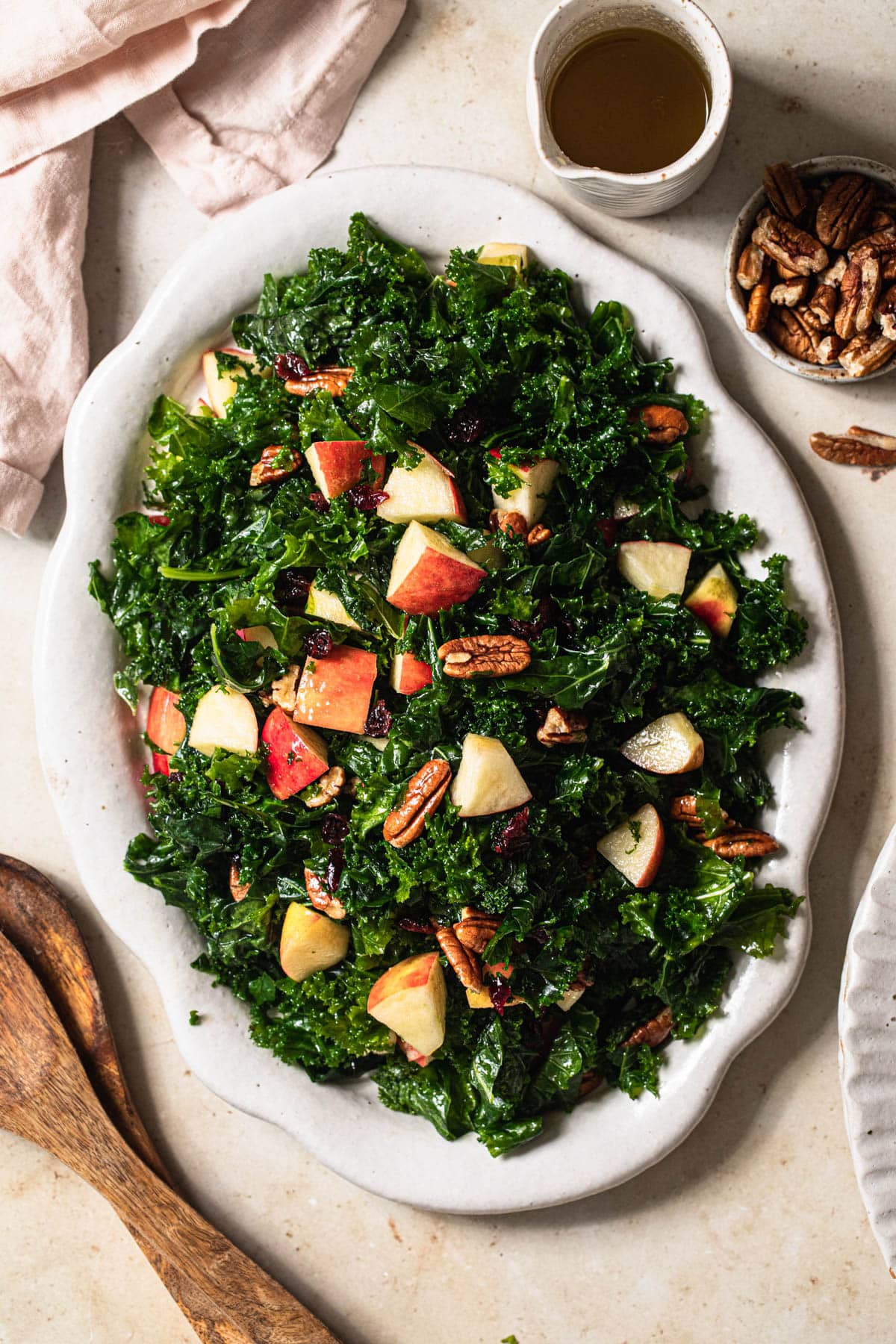 Kale, apple and cranberry salad on a white platter with dressing in a jug off to the side.
