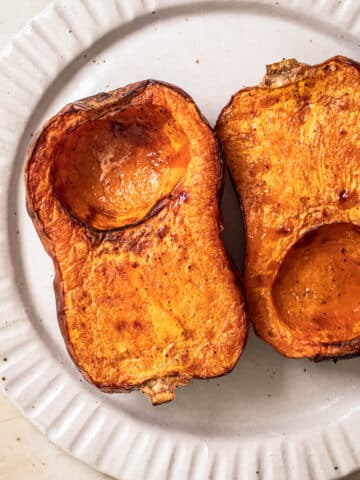 Two halves of roasted butternut squash from the air fryer on a white plate.