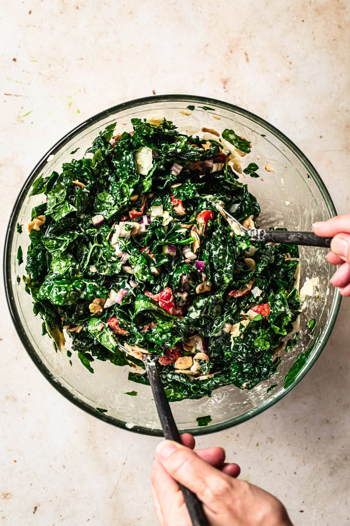 Kale salad with tahini dressing being tossed in a large glass mixing bowl.