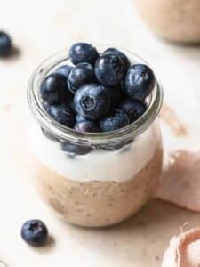 Overnight oats in a small jar topped with yoghurt and blueberries.