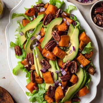 Roasted sweet potato avocado salad on a white platter with apple cider dressing in the background.