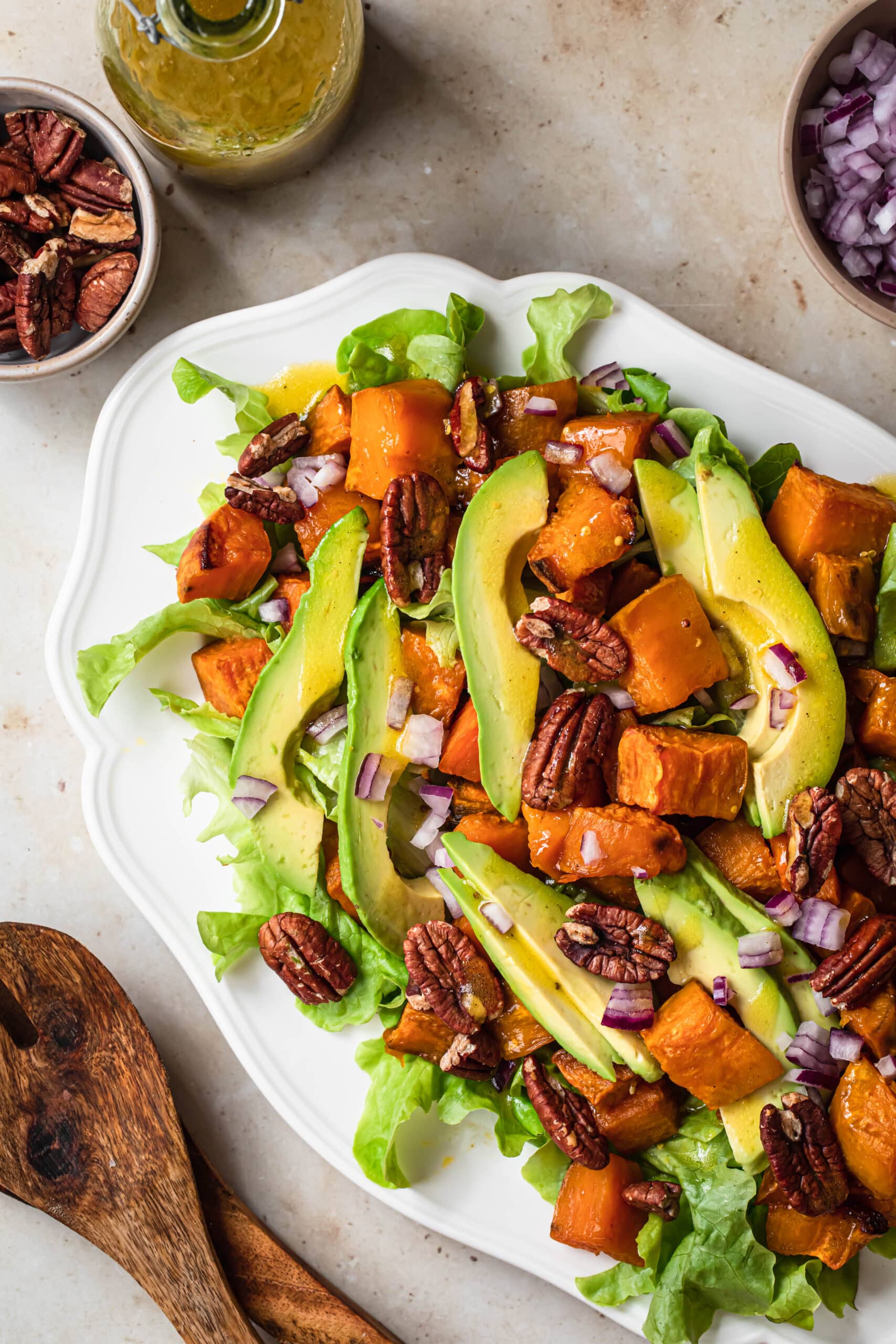 Roasted sweet potato avocado salad on a white platter with apple cider dressing in the background.