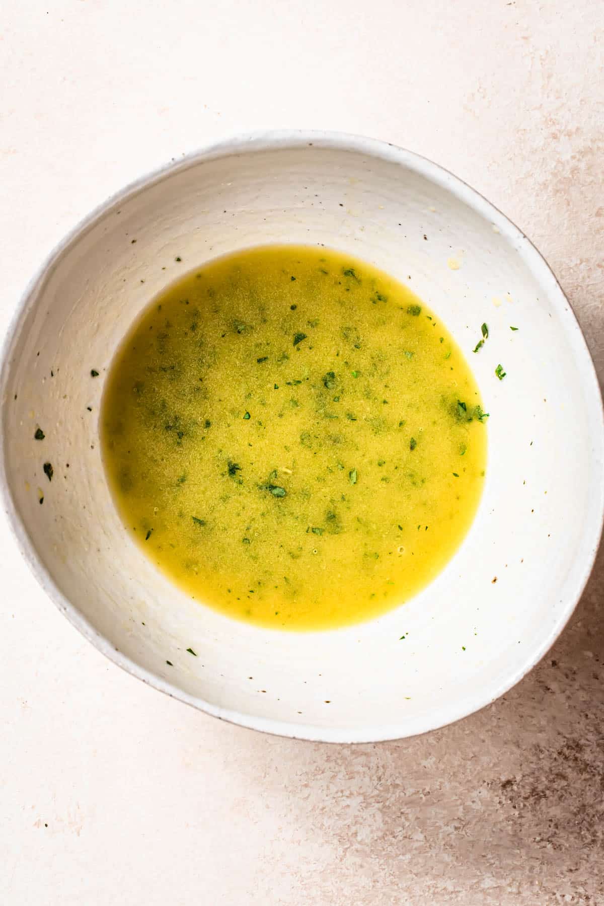 Top down image of a lemon herb dressing in a white ceramic bowl.