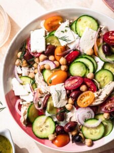 Top down, close up image of Chickpea Chicken Salad in a pink and white serving bowl, two glasses of rosé off to the side.
