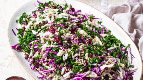 45 degree angle photo of chopped kale salad on a serving platter with ginger citrus dressing in the background.