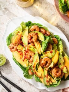Prawn and mango salad on a white platter, with a bottle of wine off to the side.