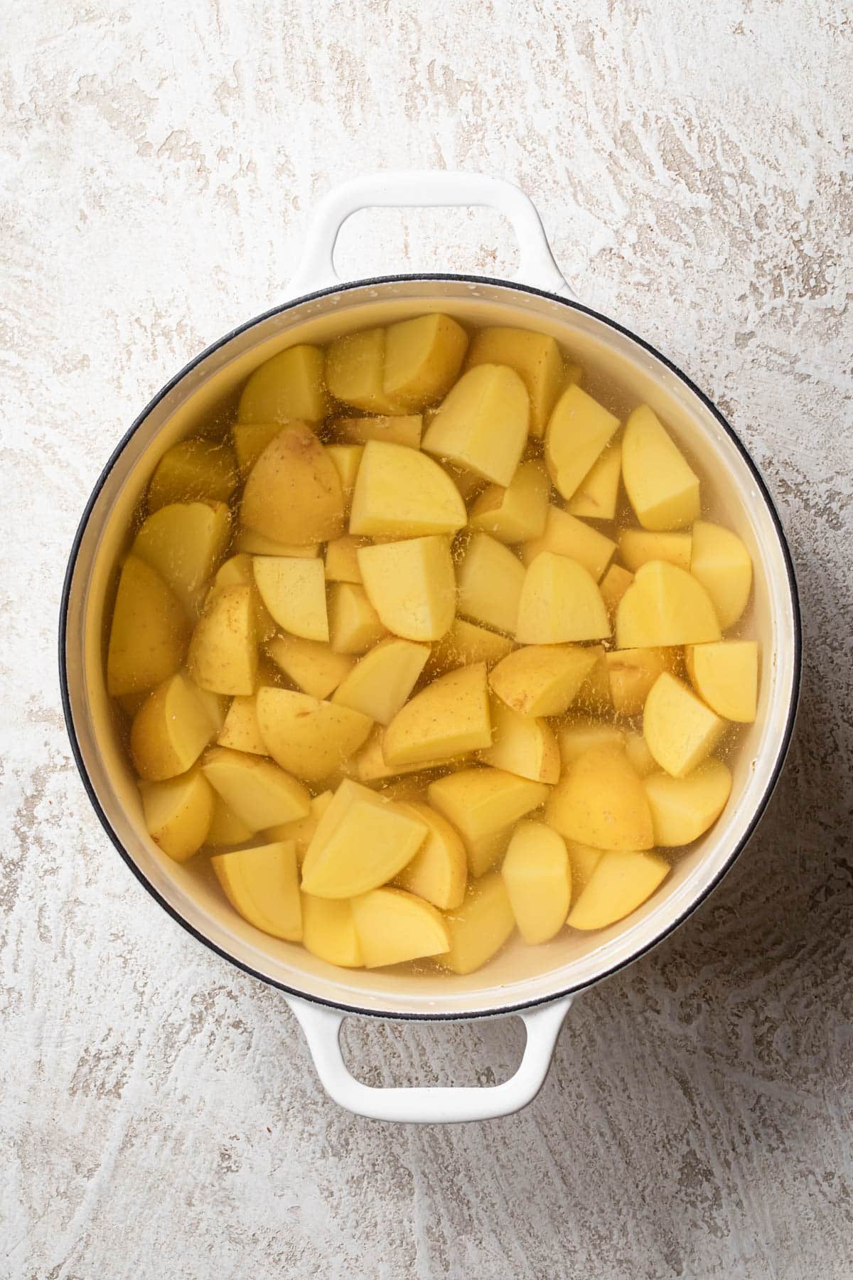 Top down photo of chopped potatoes in a large pot of water.