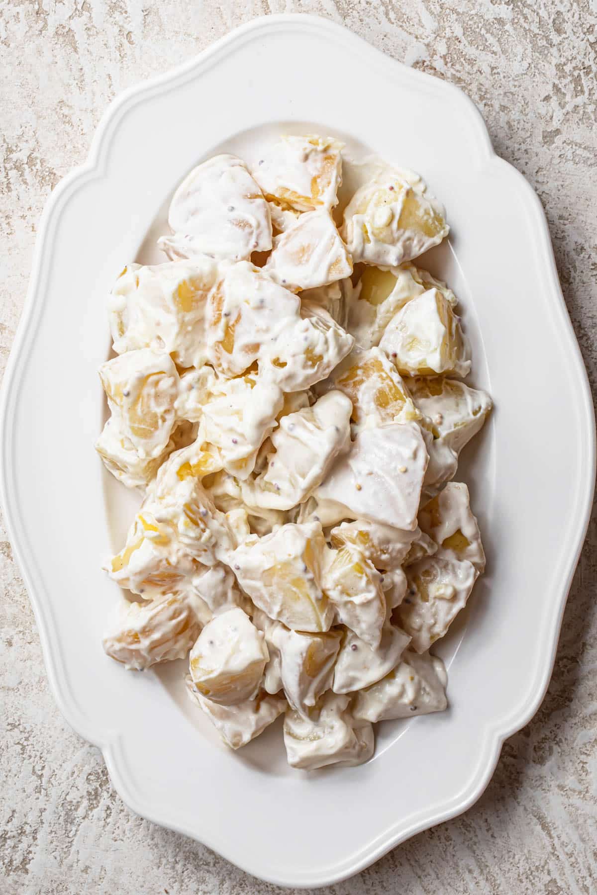 Large boiled potato chunks covered in creamy dressing on a white serving platter.