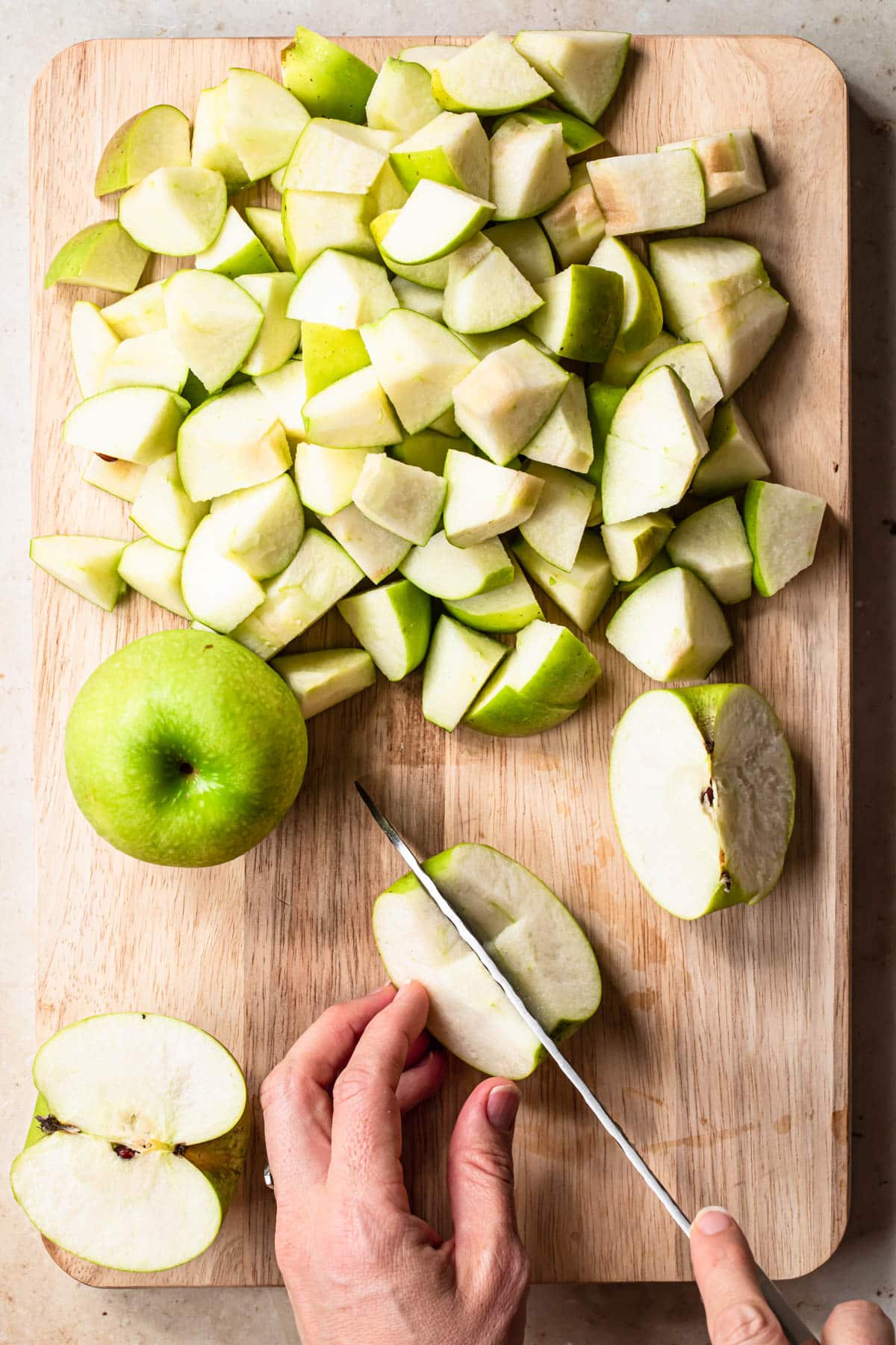 A quarter of an apple being sliced in half with a sharp knife on a timber board, to make homemade applesauce with no added sugar.