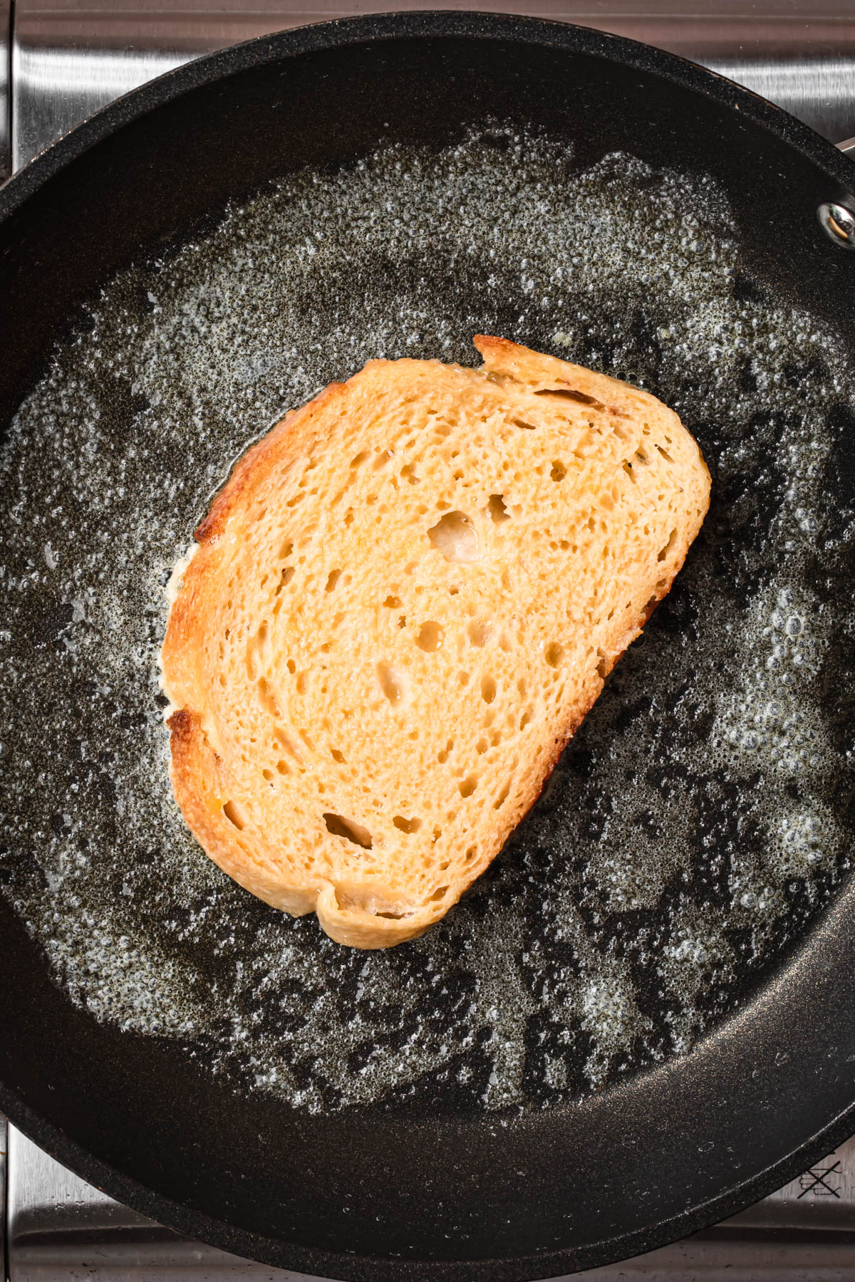 A slice of egg soaked bread added to a hot skillet.
