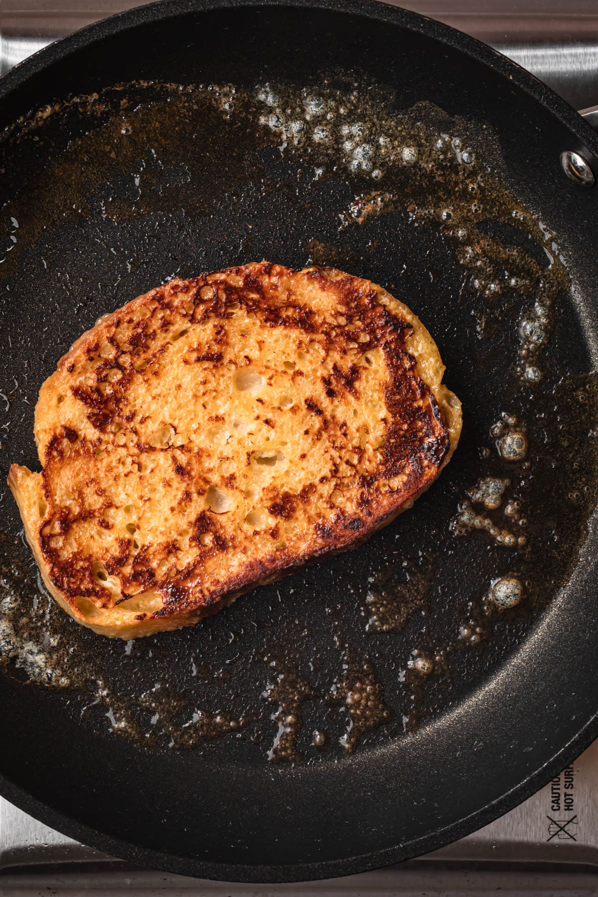 Sourdough French toast frying in a buttered, hot skillet.