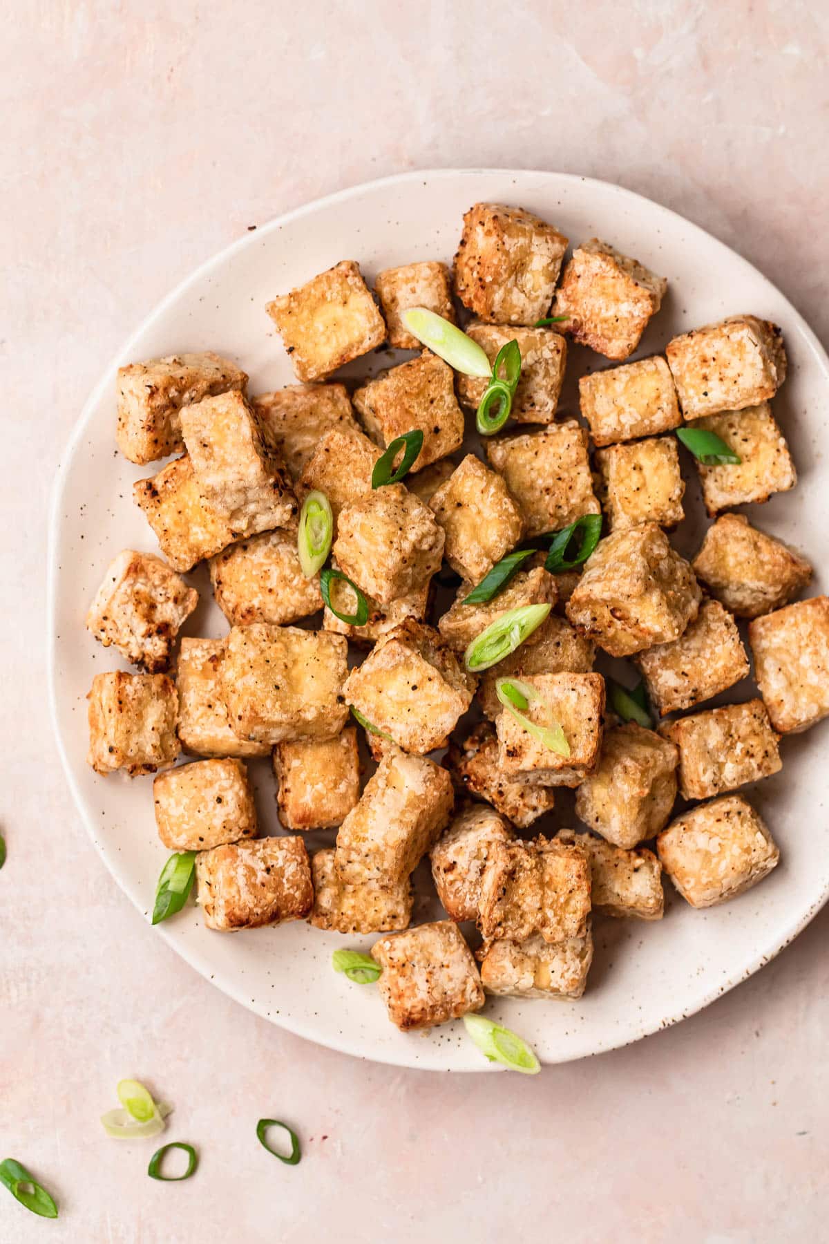 Golden brown salt and pepper tofu cooked in the air fryer, on a white plate, topped with thinly sliced green onions.