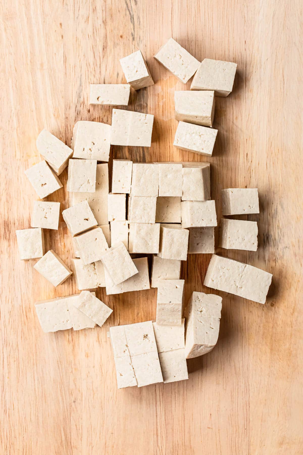 Extra firm tofu cut into cubes on a timber chopping board.