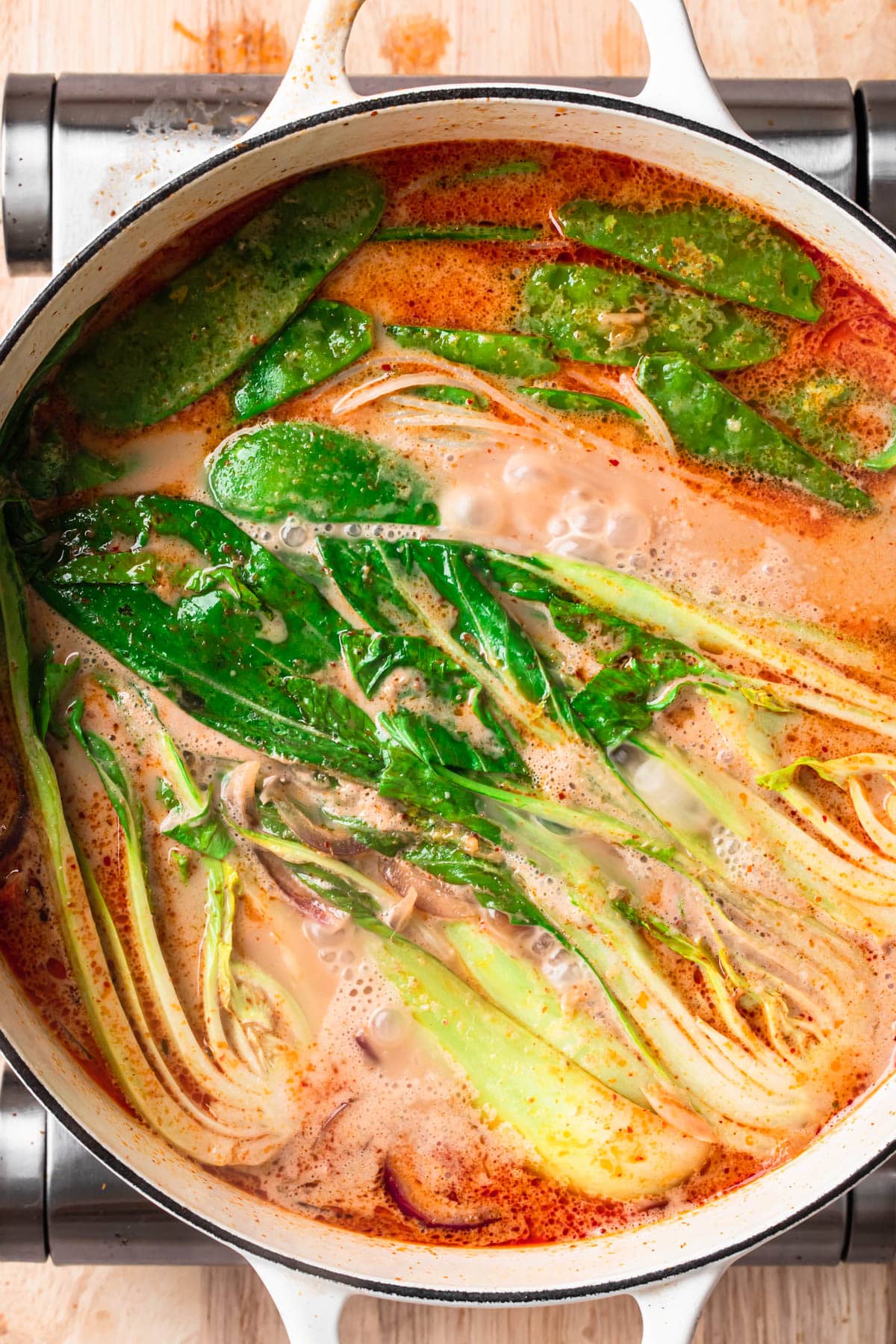 Vegetarian Thai Noodle Soup simmering in a large white soup pan, with snow peas added in.