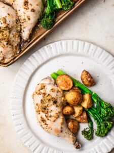 Greek chicken tray bake dinner on a white plate, with the tray to the side.