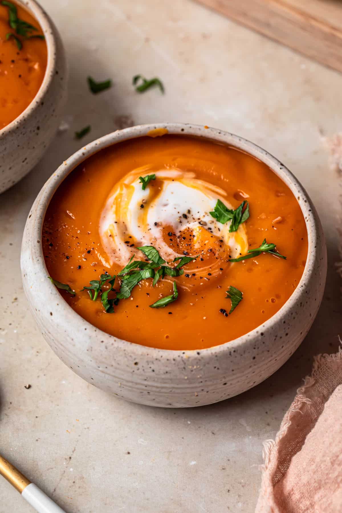 Close up photo of 3 ingredient butternut squash soup served in two small ceramic bowls, topped with yoghurt and fresh herbs.