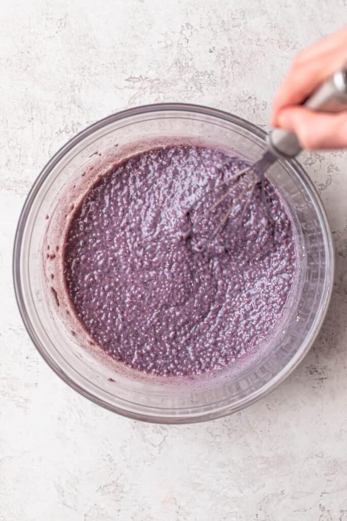 Blueberry chia pudding being mixed in a glass mixing bowl.