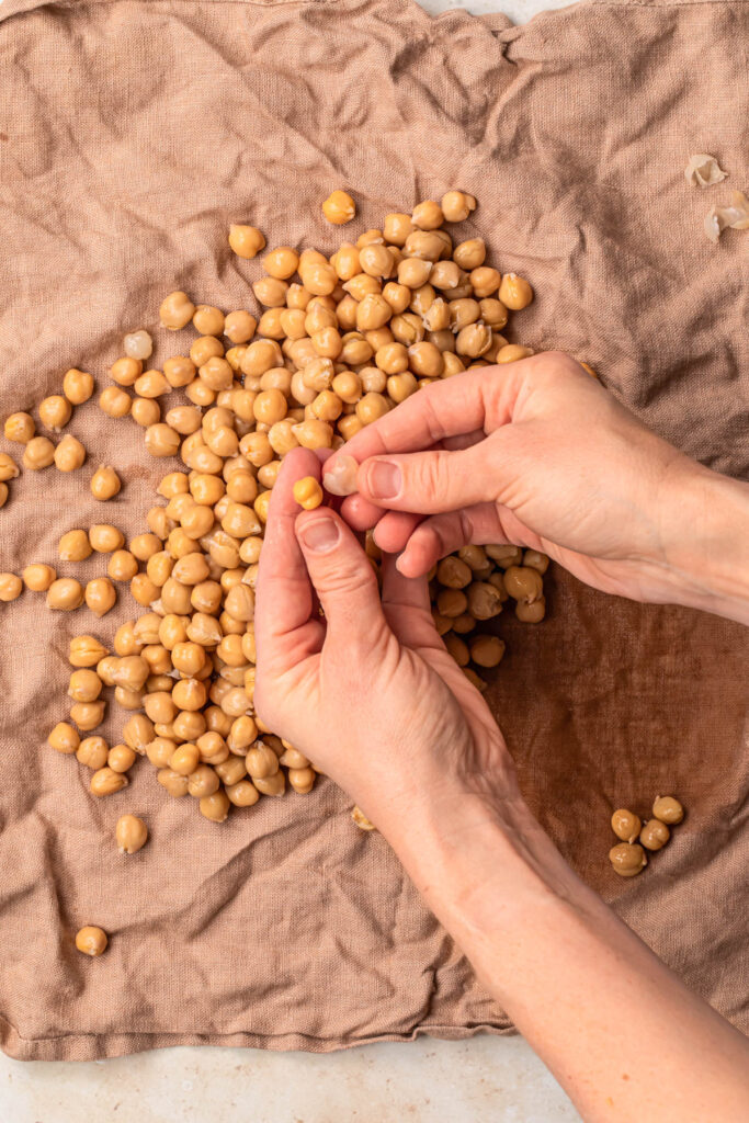 Hands picking up a chickpea and removing the skin from the chickpea.