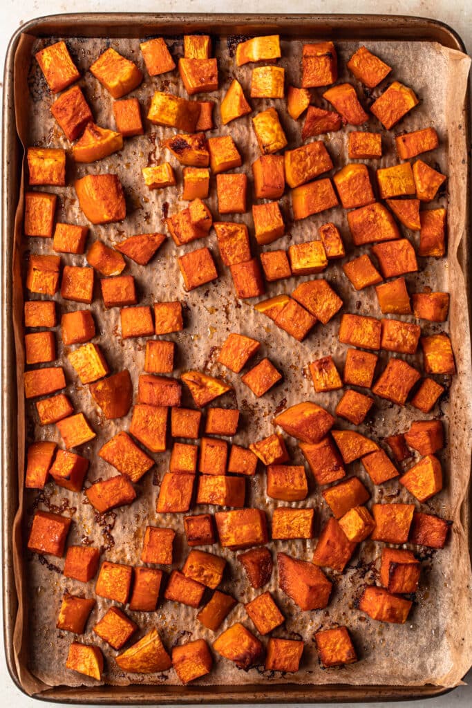 Roasted butternut squash cubes on a parchment paper lined baking tray.