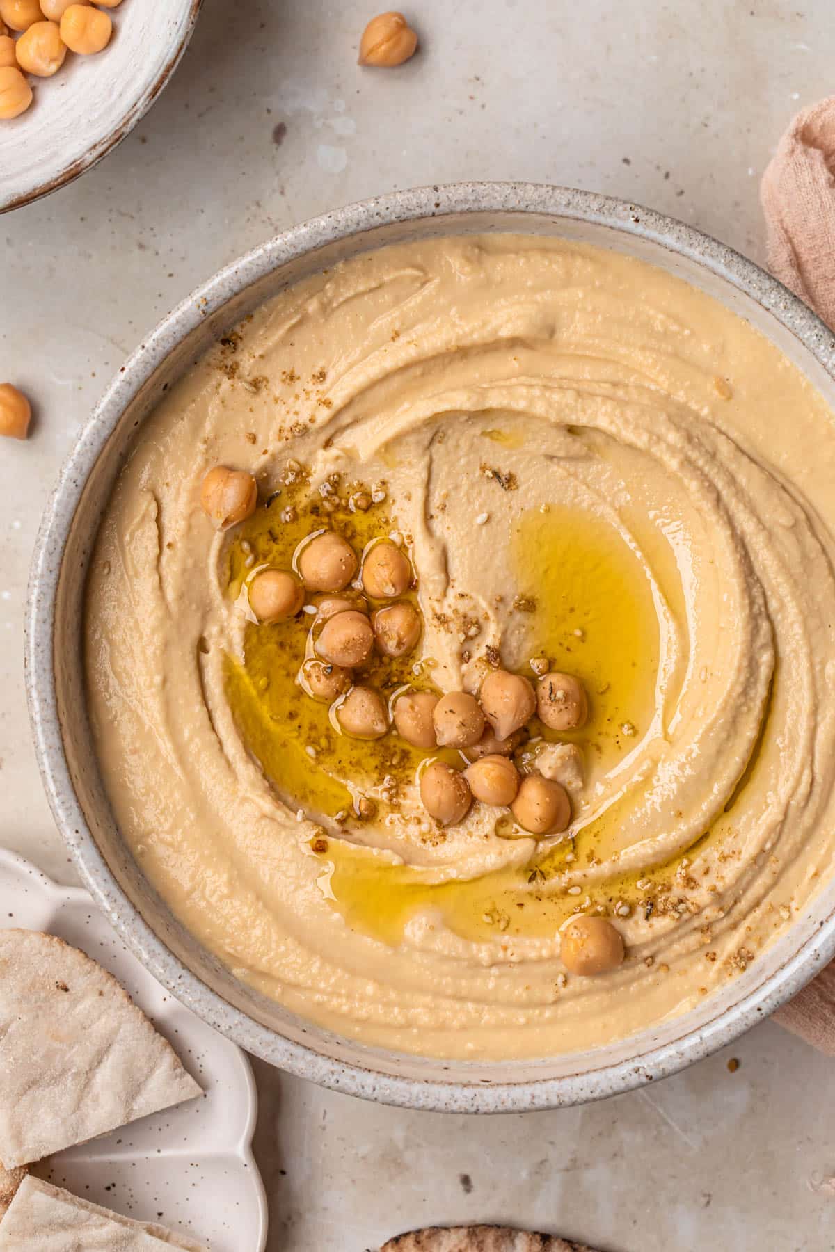 Creamy hummus in a ceramic bowl, topped with a drizzle of olive oil, chickpeas and dukkah.
