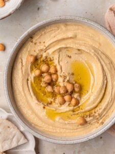 Creamy hummus in a ceramic bowl, topped with a drizzle of olive oil, chickpeas and dukkah.