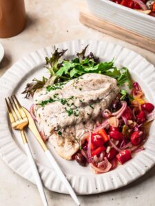 Mediterranean baked white fish on a dinner plate with baked cherry tomatoes, onions and olives.
