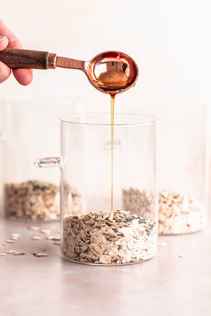 Maple syrup being poured into an oat mixture in a glass jar.