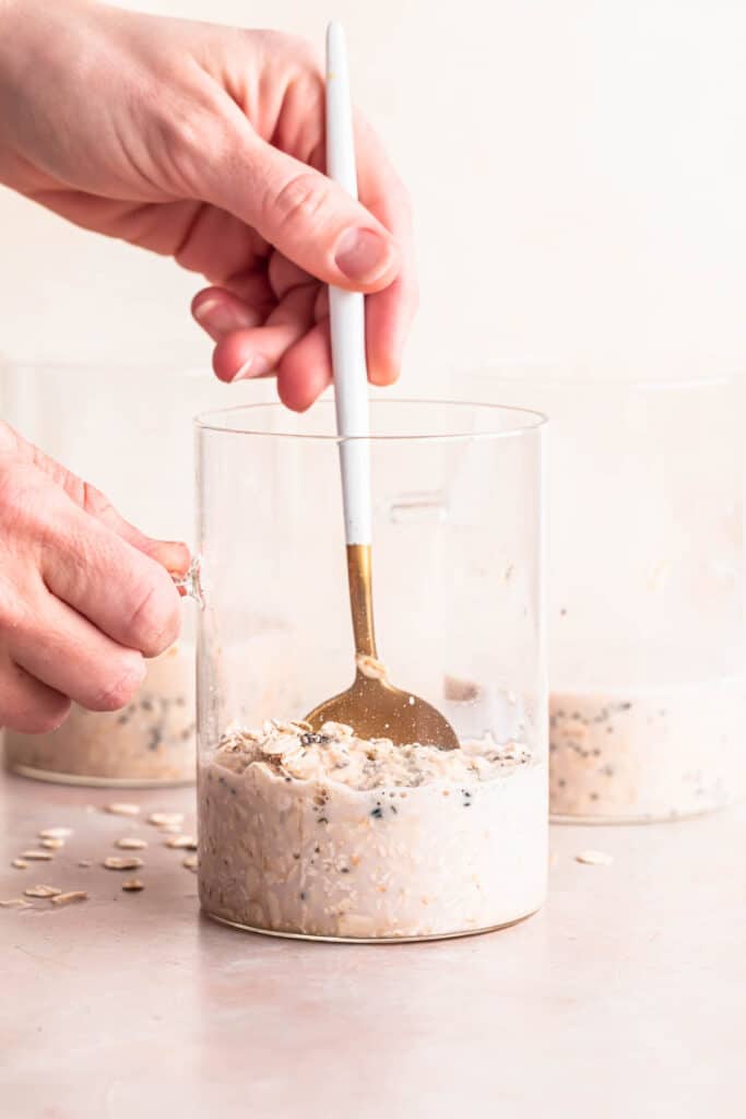 Overnight oats mixture in a glass jar being stirred with a golden spoon.