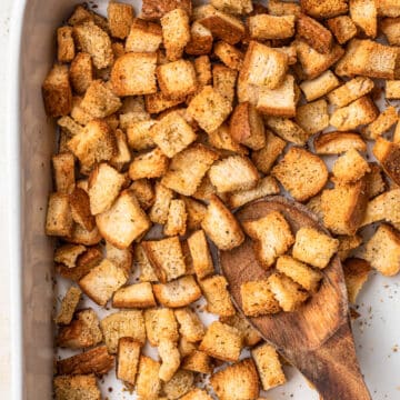 Golden brown, gluten free croutons in a white baking dish with a wooden spoon.