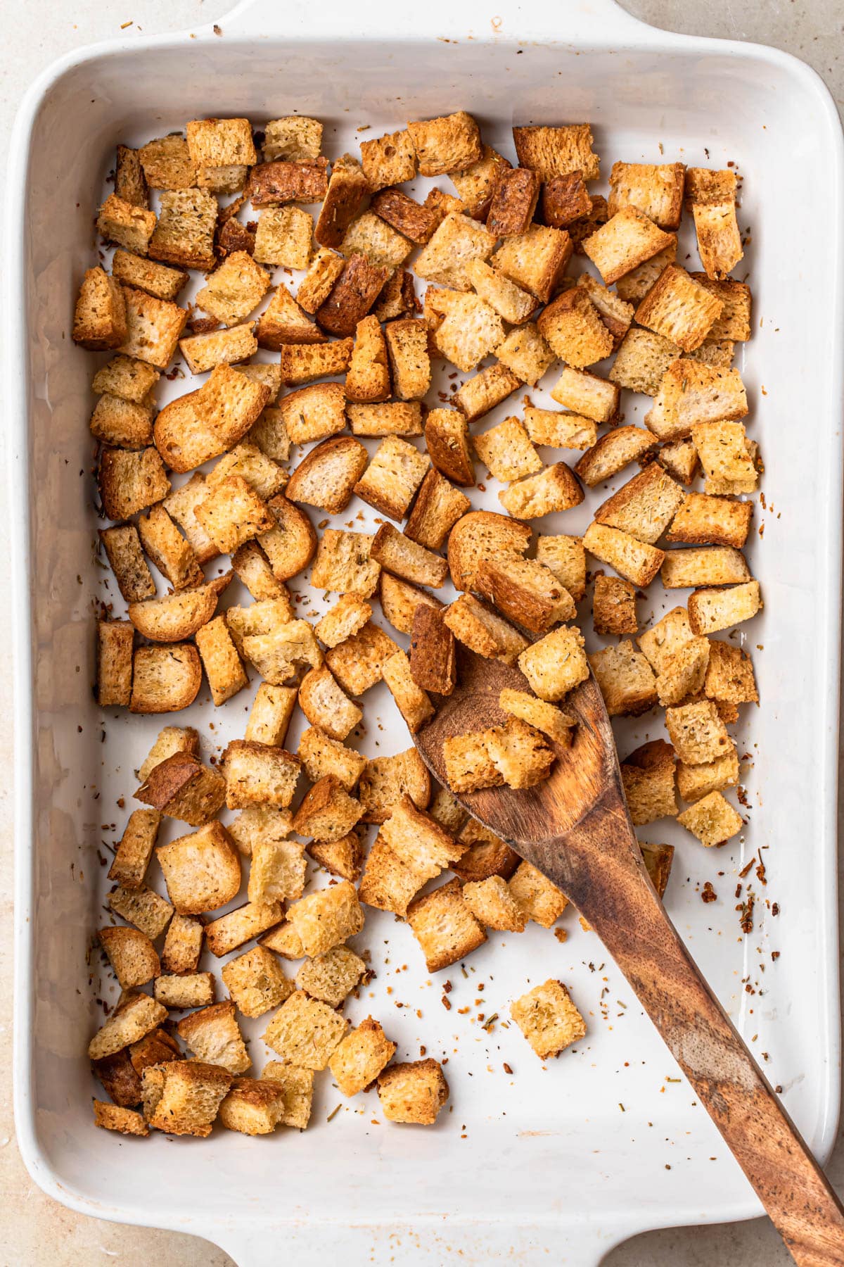 Golden brown, gluten free croutons in a white baking dish with a wooden spoon.