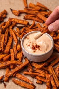 A sweet potato fry being dipped into vegan chipotle sauce.