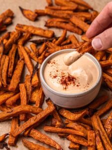 A sweet potato fry being dipped into vegan chipotle sauce.