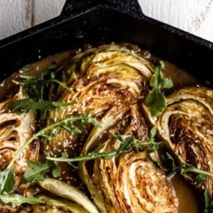 A close up shot of Miso Braised Cabbage in a cast iron pan with a sprinkle of fresh greens on top.