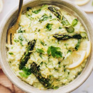 Lemon risotto with a fork inside and Asparagus set on top with herb and lemon garnish.