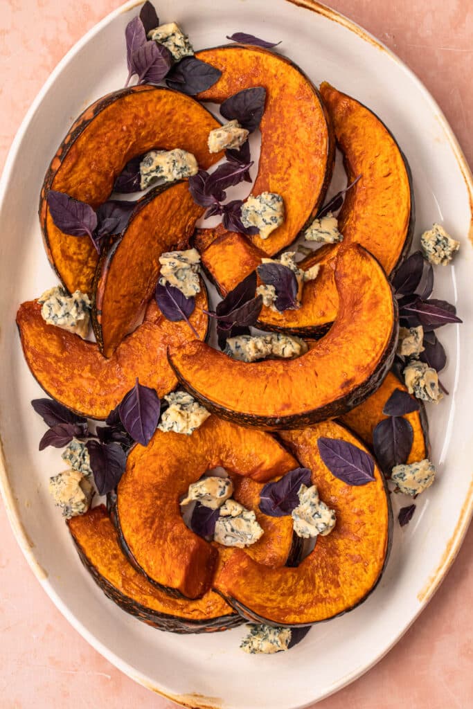Maple roasted pumpkin wedges topped with purple basil and blue cheese on a serving platter.