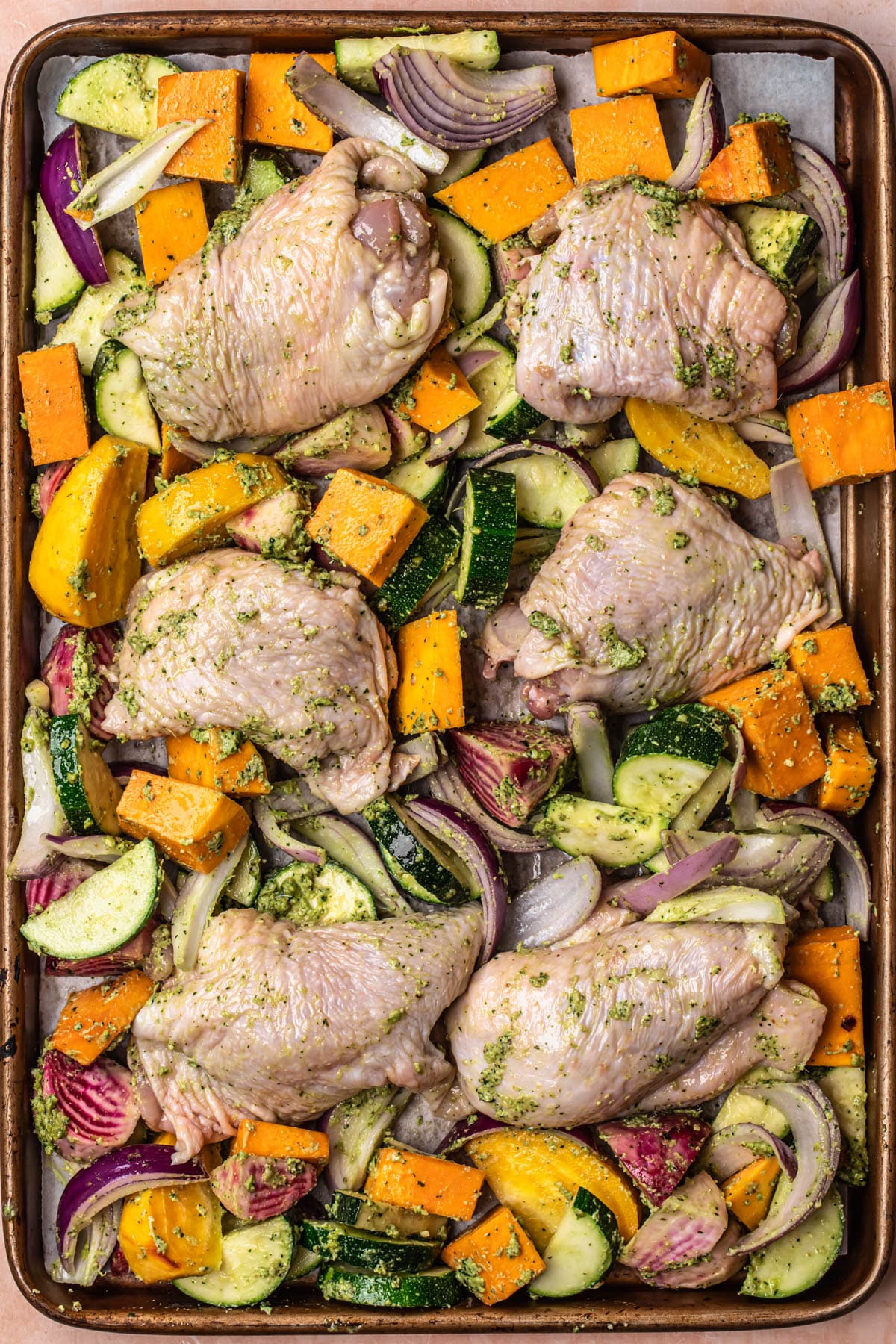Pesto marinated chicken and vegetables added to a large sheet pan.