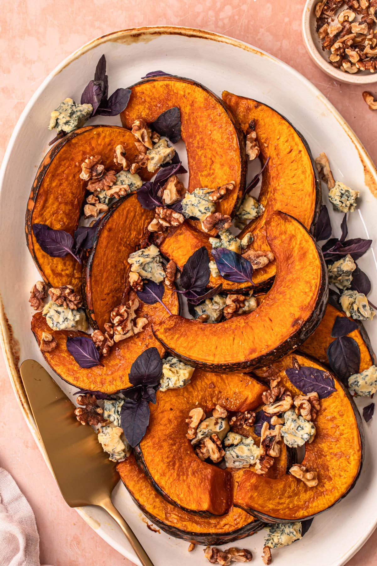 Maple roasted pumpkin wedges on a serving platter topped with soft cheese, basil and toasted walnuts.