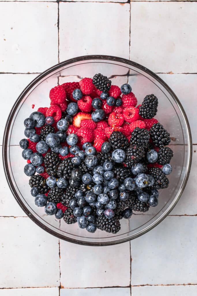 Strawberries, blueberries, raspberries and blackberries added to a large glass mixing bowl.