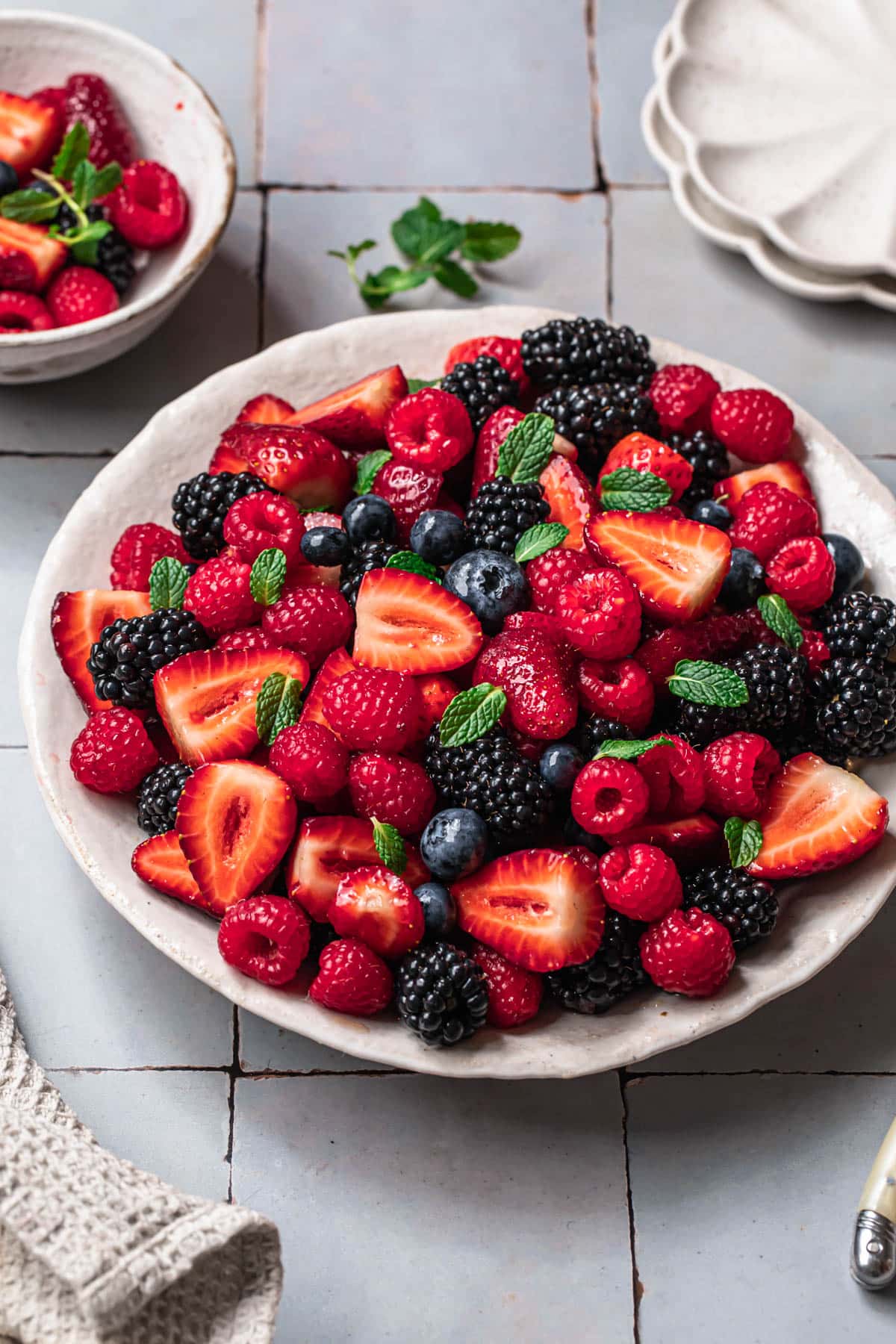 Strawberry and blueberry salad in a white serving bowl, topped with mint leaves.