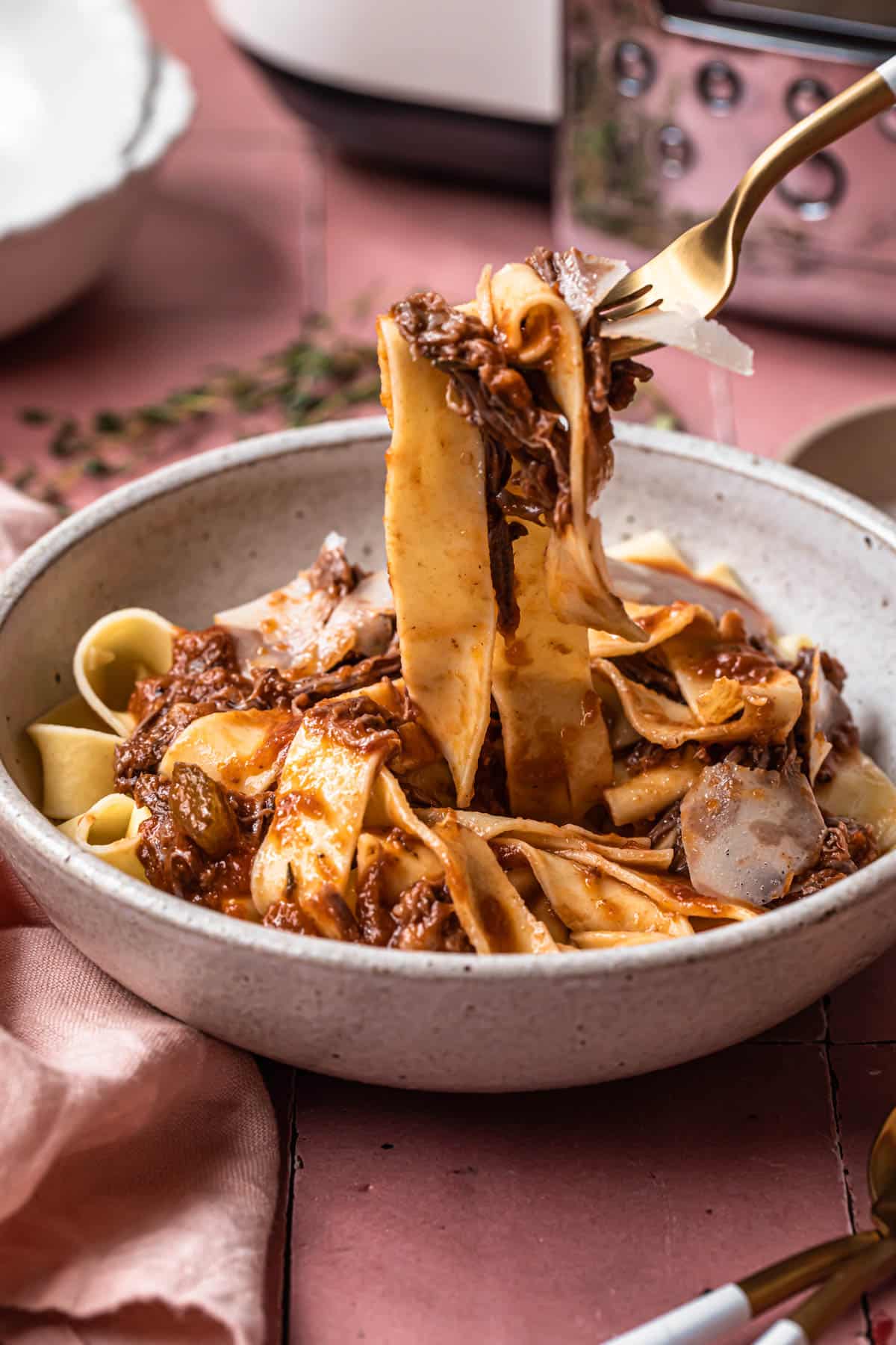 Slow cooker short rib beef ragu on parpadelle in a bowl, with a fork taking pasta out of the bowl.