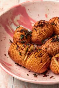 Hasselback red potatoes with a prosciutto crumb in a pink ceramic bowl.