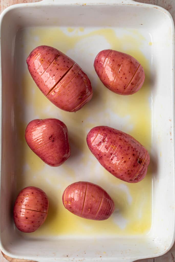 Uncooked hasselback red potatoes, coated in olive oil in an olive oil greased baking dish.