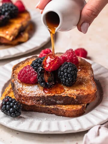 Almond milk French toast on a plate, topped with berries with maple syrup being poured over the top.