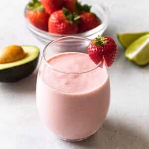 a strawberry avocado smoothie in a short glass with a strawberry garnishing the rim of the glass.