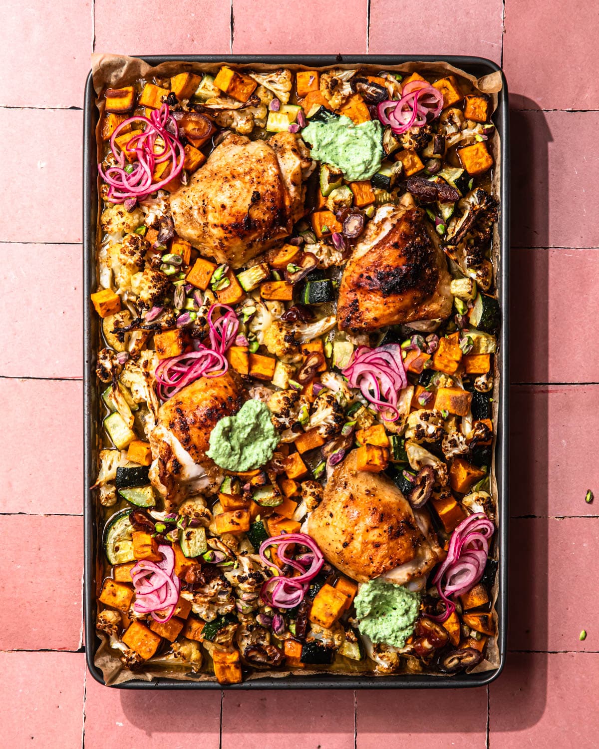 Sheet Pan Moroccan Chicken served with pickled red onions and a green tahini sauce on the pan.