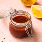 Harissa marinade in a glass jar with sliced lemons in the background.