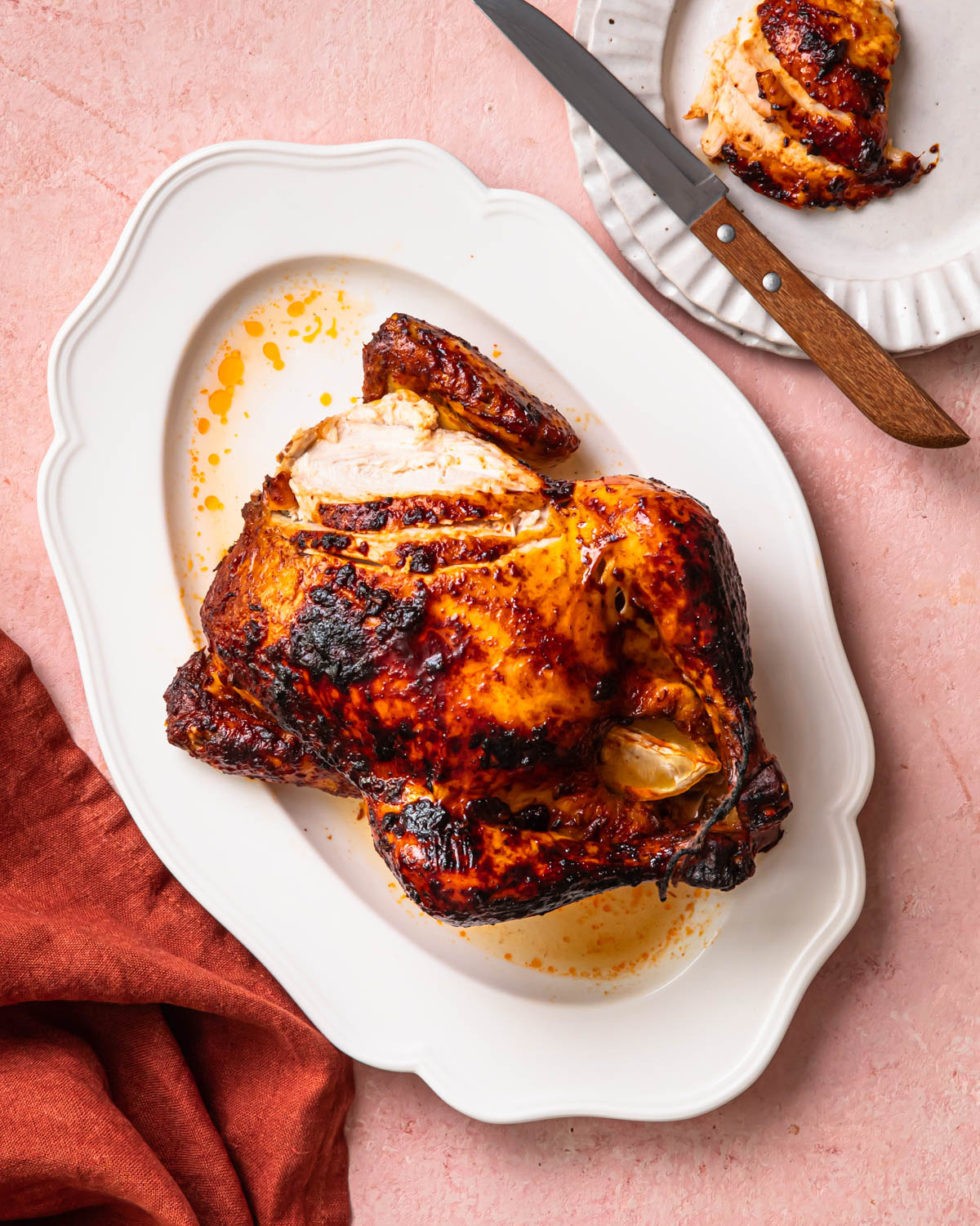 Harissa roast chicken on a serving platter with some slices cut into the breast. 