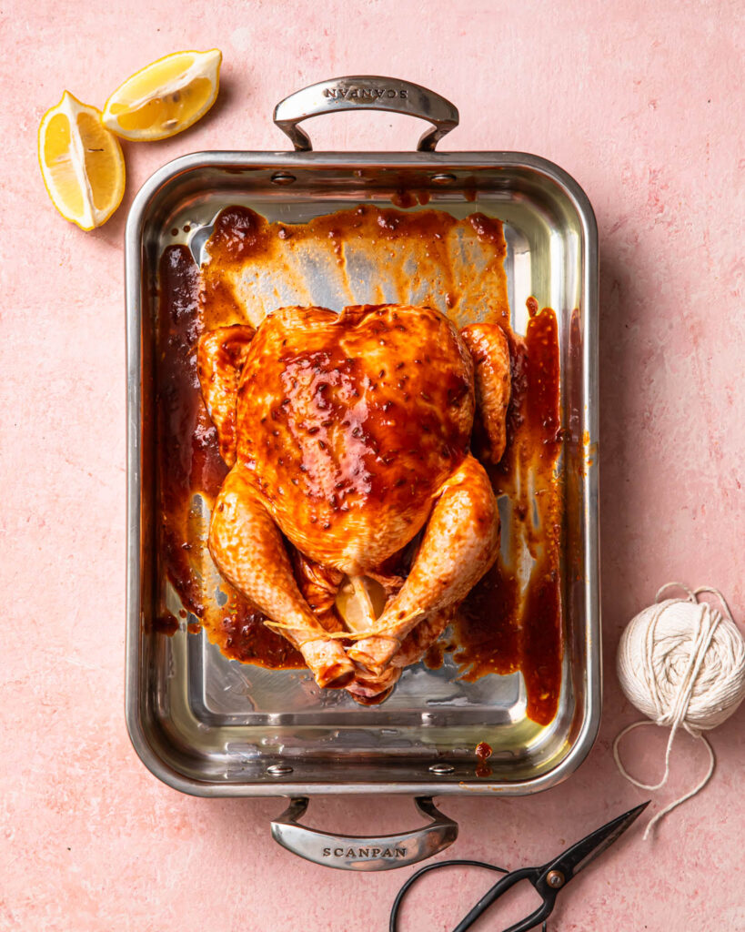 Whole chicken covered in harissa marinade. The chicken is sitting in a roasting pan.