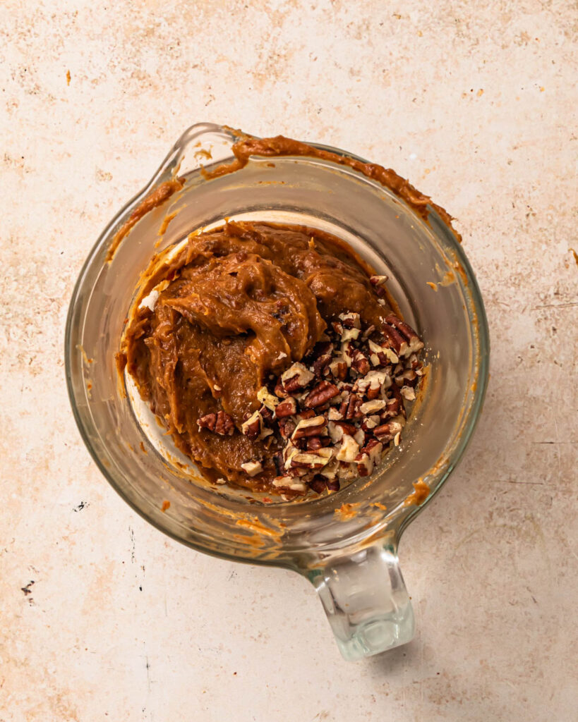 Chopped pecans added to salted date caramel in a glass jug.