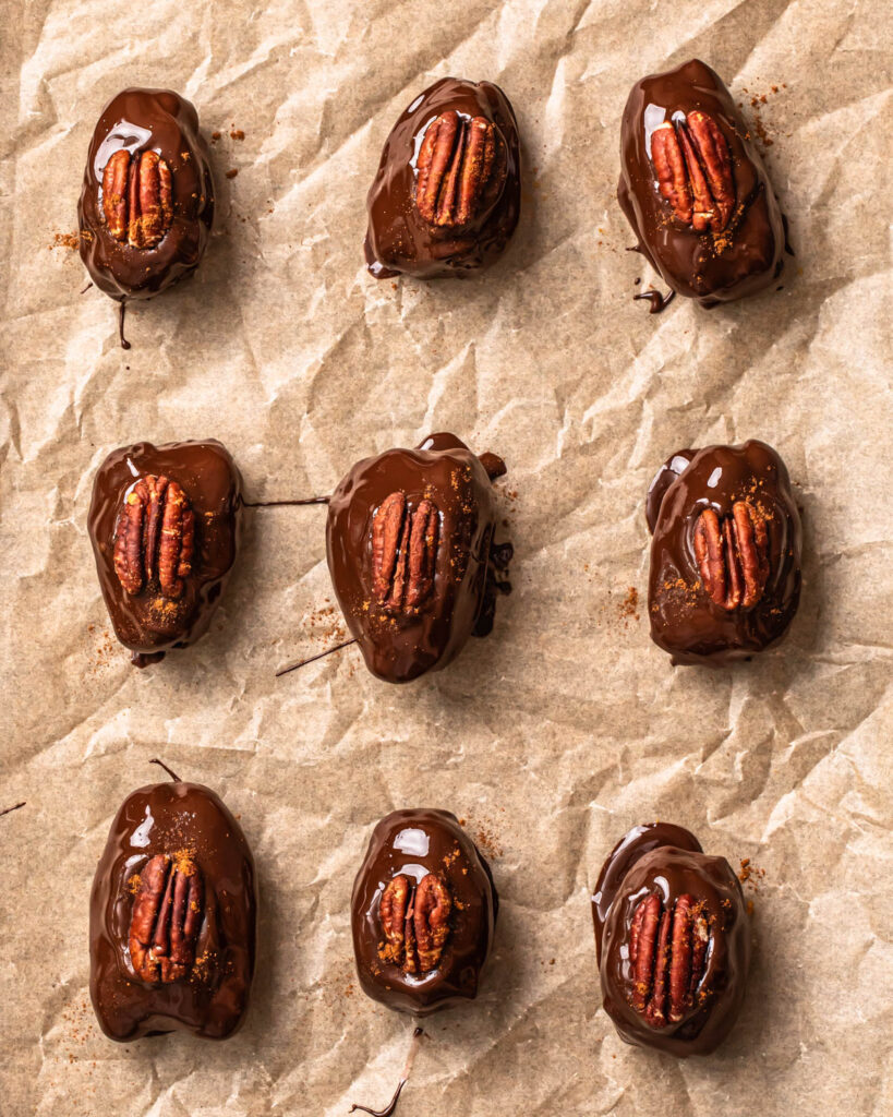 Pecan pie stuffed dates coated in melted chocolate and topped with a pecan and a dusting of cinnamon.